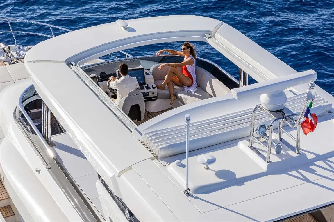 Aerial view of a modern yacht, with a woman in a red swimsuit relaxing while a man navigates at the helm.
